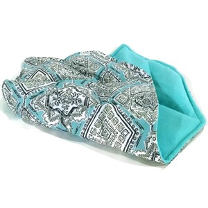A turquoise and white patterned fabric heating pad with a turquoise fleece lining. The heating pad is folded open to reveal the fleece lining.