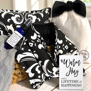 May include: A gift basket with a black and white patterned heating pad, a blue aromatherapy spray, a gray knitted item, and a white bag with a black bow. A card reads "A Warm Hug and a LIFETIME of HAPPINESS!"
