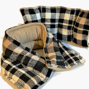 May include: A neck wrap featuring a black, white, and tan buffalo plaid pattern on the exterior. The interior lining is a solid tan color. The wrap is segmented into multiple rectangular sections and has a curved shape designed to fit around the neck.