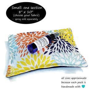 Puede incluir: Un coj&iacute;n de tela rectangular de 20,32 cm por 25,4 cm con base blanca y estampado floral en naranja, amarillo y azul. Un peque&ntilde;o frasco pulverizador azul con una etiqueta blanca que dice AromaTherapy Spritzer descansa sobre el coj&iacute;n.