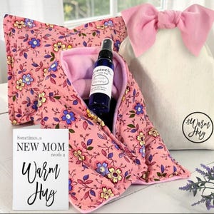 Pink gift set with bow containing microwave heating wraps, essential oil spray and a new mom greeting card.  Packaging is pictured with natural cotton gift bag and big pink bow