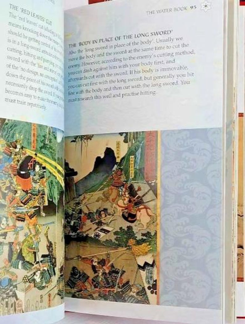 K&ouml;nnte beinhalten: Eine Seite aus einem Buch mit dem Titel "The Water Book" mit einer detaillierten Illustration einer Samurai-Schlacht. Der Text auf der Seite behandelt die Technik "Der K&ouml;rper an der Stelle des Langschwertes" im Schwertkampf.