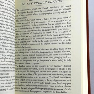 May include: An open book displaying the title "PAINE'S PREFACE TO THE FRENCH EDITION". The pages are cream-coloured with black text. The book has a brown cover and is open to page 69.