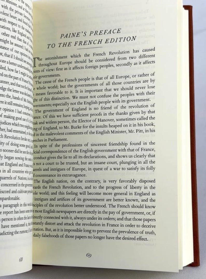 May include: An open book displaying the title "PAINE'S PREFACE TO THE FRENCH EDITION". The pages are cream-coloured with black text. The book has a brown cover and is open to page 69.
