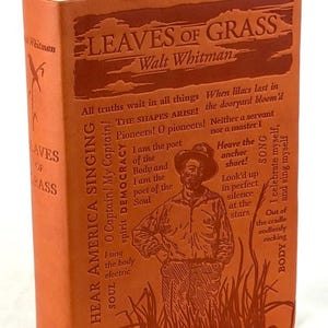 May include: A hardcover book titled "Leaves of Grass" by Walt Whitman. The cover is a reddish-orange color with embossed text and a portrait of a man. The book features excerpts from the poem.