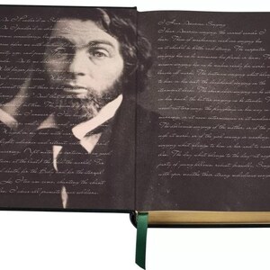 May include: An open book with a black cover and gold accents. The left page features a black and white portrait of a man with a beard. The right page features text in a light gray font. The text reads "Four American songs: The carol-chant of near.  Place of moorhens and one singing the star-shaped in the river rust along. The carpenter singing how he remembers the frame for dawn. The woman singing how she remembers the frame for dawn. The river of words. The mother singing what belongs to her in the boat. The grandchild singing on the stream in the boat. The fisherman singing on the salt-marsh beach. The bird singing as we stand at the water's edge. The frog singing as he sits in the mud. The turtle singing as he swims away. The morning is at noon. Intermission is at midnight. The river-song of the mother, or of the young wife at water, or at the year showing as waking. Each singing what belongs to him or to her, until night stars. The day what belongs to the day, to night the purity of pang ritornello, robust, dinnacle. Singing with open mouths their strong mellifluous songs."