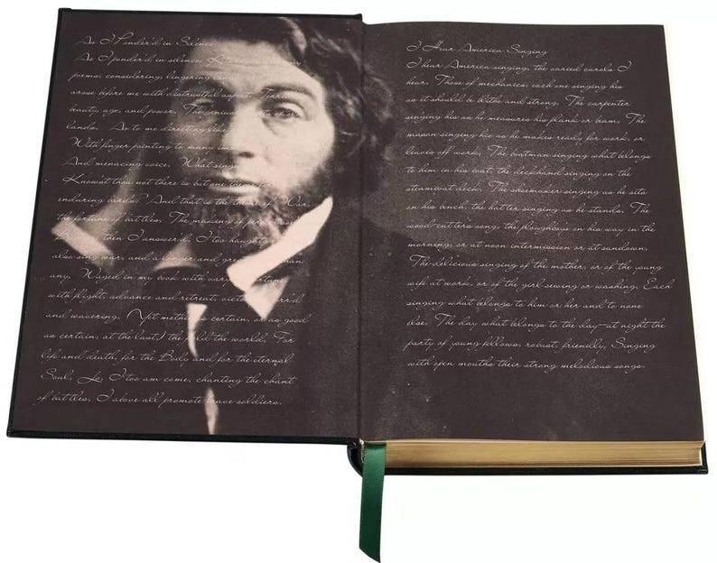 May include: An open book with a black cover and gold accents. The left page features a black and white portrait of a man with a beard. The right page features text in a light gray font. The text reads "Four American songs: The carol-chant of near.  Place of moorhens and one singing the star-shaped in the river rust along. The carpenter singing how he remembers the frame for dawn. The woman singing how she remembers the frame for dawn. The river of words. The mother singing what belongs to her in the boat. The grandchild singing on the stream in the boat. The fisherman singing on the salt-marsh beach. The bird singing as we stand at the water's edge. The frog singing as he sits in the mud. The turtle singing as he swims away. The morning is at noon. Intermission is at midnight. The river-song of the mother, or of the young wife at water, or at the year showing as waking. Each singing what belongs to him or to her, until night stars. The day what belongs to the day, to night the purity of pang ritornello, robust, dinnacle. Singing with open mouths their strong mellifluous songs."
