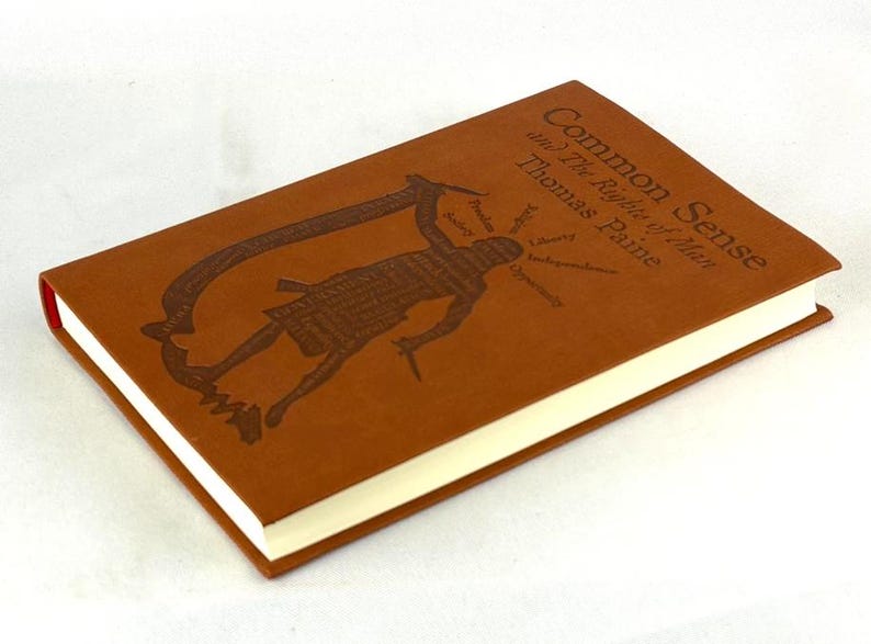 May include: A brown hardcover book titled "Common Sense and The Rights of Man" by Thomas Paine. The cover features a debossed illustration of a figure and text. The book has cream-coloured pages and a red spine.