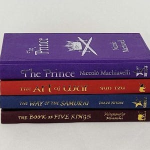 May include: A stack of five books with purple, red, blue, and maroon covers. The titles are "The Prince" by Niccol&ograve; Machiavelli, "The Art of War" by Sun Tzu, "The Way of the Samurai" by Inazo Nitobe, and "The Book of Five Rings" by Miyamoto Musashi.