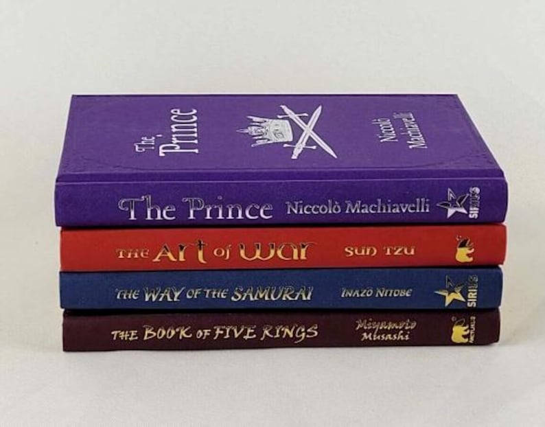 May include: A stack of five books with purple, red, blue, and maroon covers. The titles are "The Prince" by Niccol&ograve; Machiavelli, "The Art of War" by Sun Tzu, "The Way of the Samurai" by Inazo Nitobe, and "The Book of Five Rings" by Miyamoto Musashi.