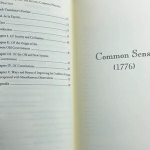 May include: An open book with text. The left page has a list of chapter titles and page numbers. The right page shows "Common Sense (1776)" in black font. The book has a brown cover and cream-coloured pages.