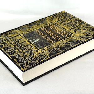May include: A hardcover book titled "Prophecies, Myths & Oracles" with a black cover and gold embossed lettering and designs. The book has white pages and black edges.
