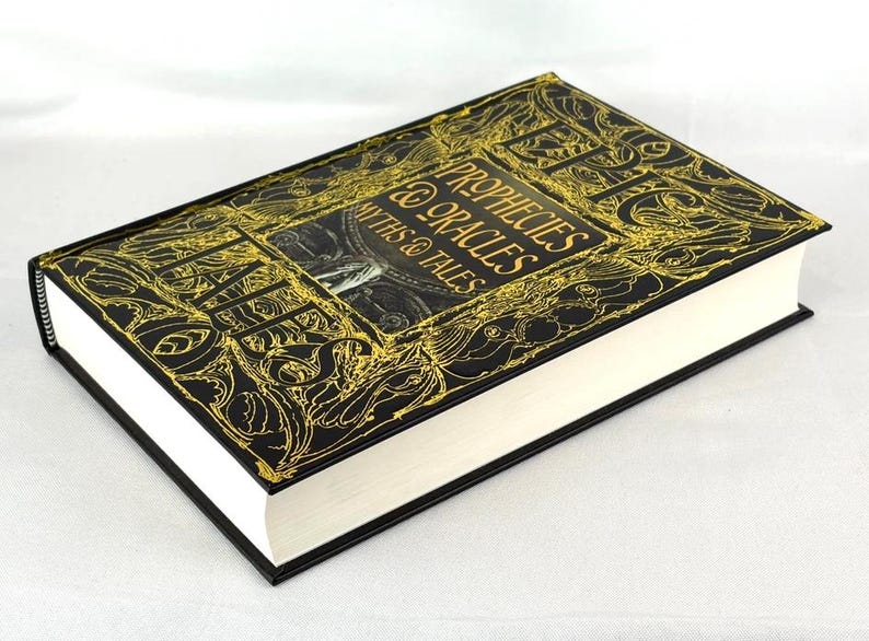 May include: A hardcover book titled "Prophecies, Myths & Oracles" with a black cover and gold embossed lettering and designs. The book has white pages and black edges.