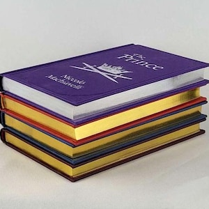 May include: A stack of five books with purple, gold, red, blue, and gold covers. The top book has the title "The Prince" and the author "Niccol&ograve; Machiavelli" printed on the cover.