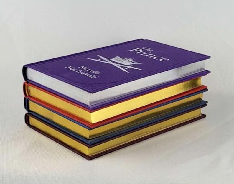 May include: A stack of five books with purple, gold, red, blue, and gold covers. The top book has the title "The Prince" and the author "Niccol&ograve; Machiavelli" printed on the cover.