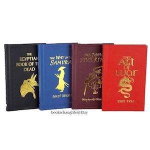 May include: Four small hardcover books with gold lettering and illustrations on the covers. The books are titled "The Egyptian Book of the Dead", "The Way of the Samurai", "The Book of Five Rings", and "The Art of War".