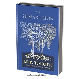 May include: The Silmarillion by J.R.R. Tolkien, a hardcover book with a blue cover featuring a gold illustration of two trees with intricate details. The title "The Silmarillion" is printed in gold lettering on the cover.