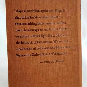 May include: A brown book with a quote from Barack Obama about hope. The quote reads, "Hope is not blind optimism. Hope is that thing inside us that insists... that something better awaits us if we have the courage to reach for it and to work for it and to fight for it. Hope is the bedrock of this nation. We are not a collection of red states and blue states. We are the United States of America."