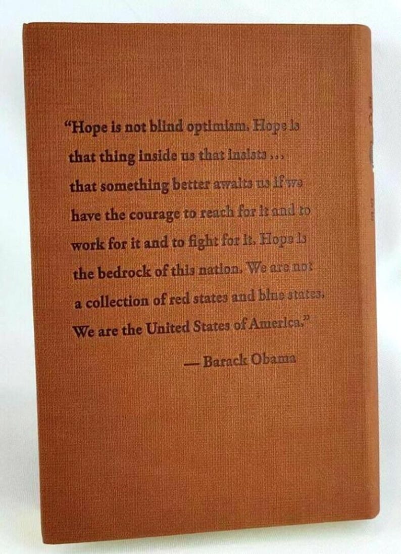 May include: A brown book with a quote from Barack Obama about hope. The quote reads, "Hope is not blind optimism. Hope is that thing inside us that insists... that something better awaits us if we have the courage to reach for it and to work for it and to fight for it. Hope is the bedrock of this nation. We are not a collection of red states and blue states. We are the United States of America."