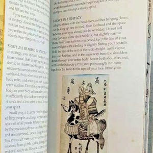 K&ouml;nnte beinhalten: Eine Schwarzwei&szlig;illustration eines Samurai-Kriegers zu Pferd. Der Krieger tr&auml;gt eine R&uuml;stung und einen Helm mit einem Wappen. Das Pferd tr&auml;gt einen Sattel und hat ein geflecktes Muster. Die Illustration ist von japanischem Text umgeben.