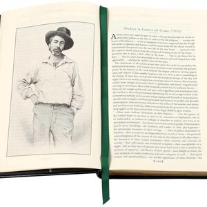 May include: An open book with a black leather cover and green ribbon bookmark. The book is open to a page with a black and white illustration of a man wearing a hat and a dark shirt. The text on the page is a preface to "Leaves of Grass" by Walt Whitman.