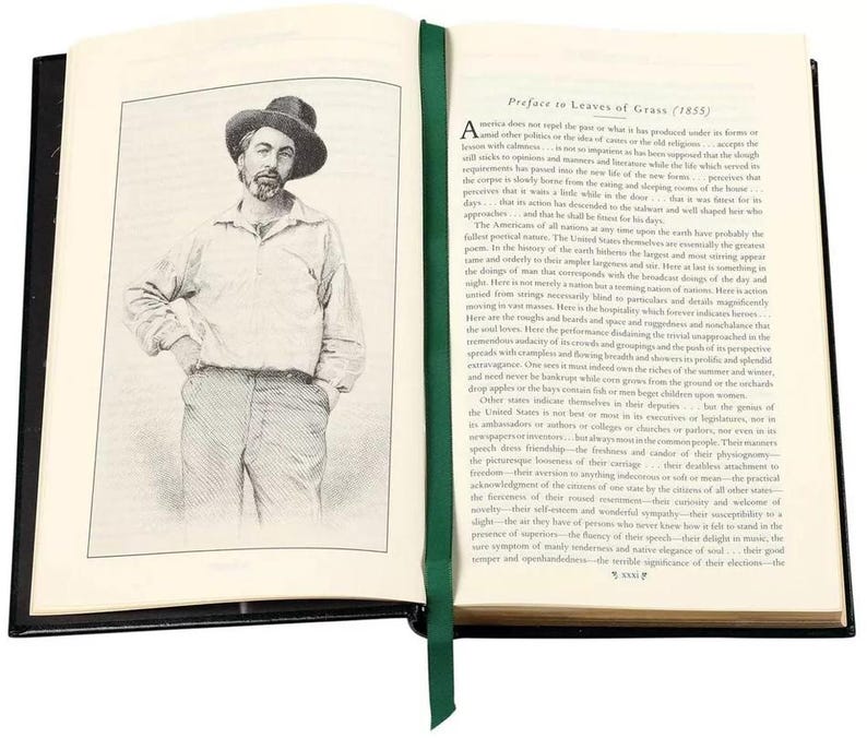 May include: An open book with a black leather cover and green ribbon bookmark. The book is open to a page with a black and white illustration of a man wearing a hat and a dark shirt. The text on the page is a preface to "Leaves of Grass" by Walt Whitman.