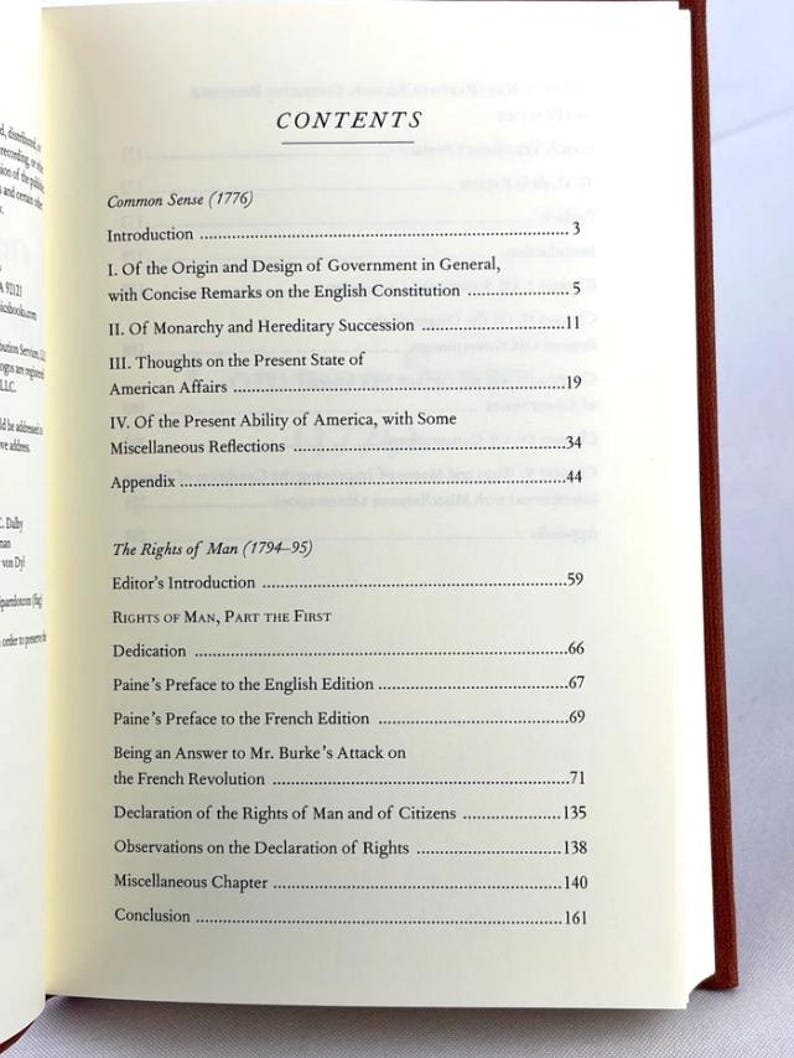 May include: An open book displaying the contents page. Titles include "Common Sense (1776)" and "The Rights of Man (1794-95)". The book's spine is red.