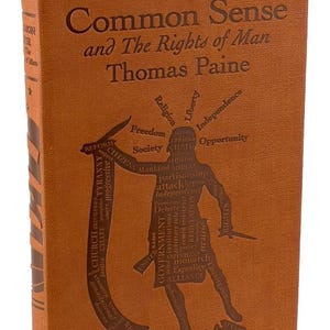 May include: A brown hardcover book titled "Common Sense and The Rights of Man" by Thomas Paine. The cover features embossed text and a graphic of a figure with knives, surrounded by words such as "Freedom" and "Government".