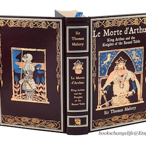 May include: A leather-bound book titled "Le Morte d'Arthur: King Arthur and the Knights of the Round Table" by Sir Thomas Malory. The cover features a gold-embossed illustration of a knight in armor.