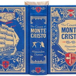 May include: A blue hardcover book with gold accents and a title that reads "The Count of Monte Cristo" by Alexandre Dumas. The cover features a ship sailing on the sea, two figures fencing, and a crest with a cross.