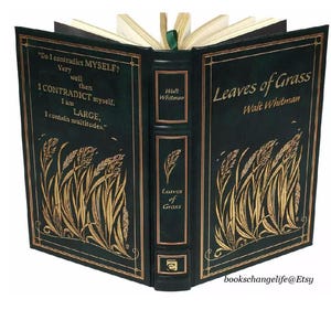 May include: A green leather-bound book with gold lettering titled "Leaves of Grass" by Walt Whitman. The cover features a gold illustration of blades of grass.