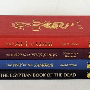 May include: A stack of five hardcover books with gold lettering on the spines. The titles are "The Art of War", "The Art of War", "The Book of Five Rings", "The Way of the Samurai", and "The Egyptian Book of the Dead".