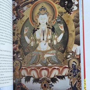 K&ouml;nnte beinhalten: Offenes Buch mit einer detaillierten Illustration einer sitzenden Figur mit mehreren Armen, umgeben von verzierten Gold- und Braunt&ouml;nen. Die Figur hat helle Haut und tr&auml;gt eine Krone. Der Text auf der linken Seite lautet "THE THIRTEENTH DAY".