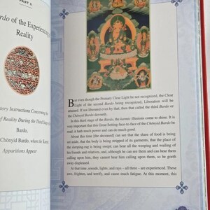 K&ouml;nnte beinhalten: Offenes Buch mit Text und einer farbenfrohen Illustration. Die Illustration zeigt eine zentrale Figur, umgeben von anderen Figuren in sitzender Position. Der Text enth&auml;lt den Titel "Bardo of the Experiencing Reality" und die Seitenzahl 39.