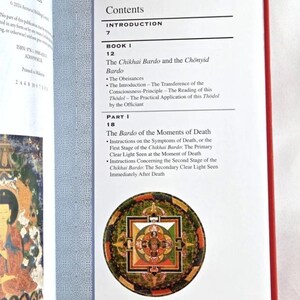 K&ouml;nnte beinhalten: Aufgeschlagenes Buch mit rotem Buchr&uuml;cken, das Inhaltsverzeichnis zeigend. Der Text enth&auml;lt "The Chikhai Bardo and the Ch&ouml;nyid Bardo" und "The Bardo of the Moments of Death". Eine farbenfrohe kreisf&ouml;rmige Illustration ist abgebildet.