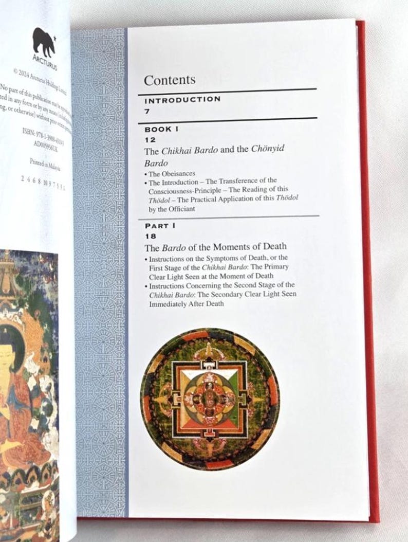K&ouml;nnte beinhalten: Aufgeschlagenes Buch mit rotem Buchr&uuml;cken, das Inhaltsverzeichnis zeigend. Der Text enth&auml;lt "The Chikhai Bardo and the Ch&ouml;nyid Bardo" und "The Bardo of the Moments of Death". Eine farbenfrohe kreisf&ouml;rmige Illustration ist abgebildet.