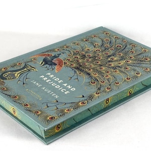 May include: A white ceramic mug with a black handle and the text "But First, Coffee" in a black, bold font. The mug is sitting on a white surface. The mug is approximately 4 inches tall.