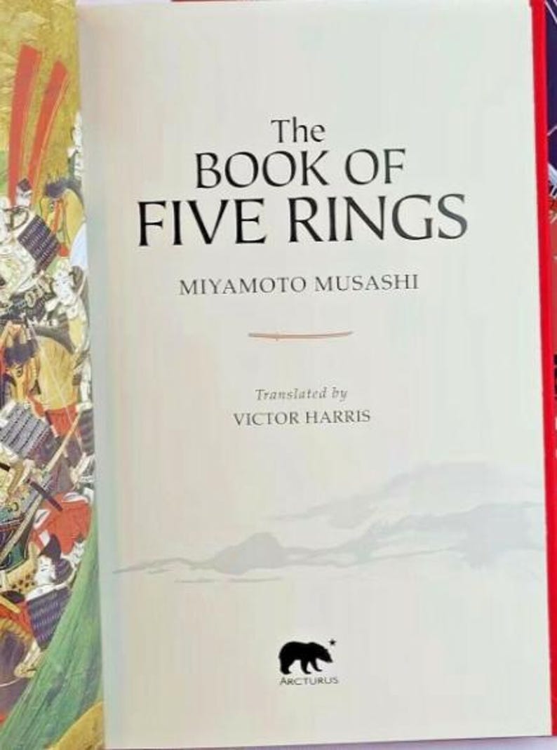 K&ouml;nnte beinhalten: Das Buch der F&uuml;nf Ringe von Miyamoto Musashi, &uuml;bersetzt von Victor Harris. Der Buchumschlag zeigt eine Schwarzwei&szlig;illustration eines B&auml;ren mit einem Stern dar&uuml;ber und dem Wort "Arcturus" darunter.