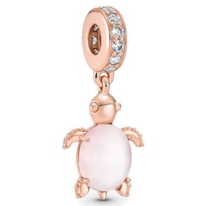 May include: Rose gold-toned charm featuring a sea turtle design. The turtle has a light pink, oval-shaped body and detailed flippers and head. The charm includes a ring adorned with clear crystals for attachment to a bracelet or necklace.