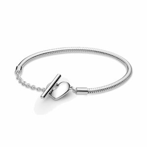 May include: A silver bracelet with a heart-shaped clasp and a T-bar closure. The bracelet has a snake chain design and a small chain connecting the clasp to the bracelet. The heart clasp is smooth and polished.