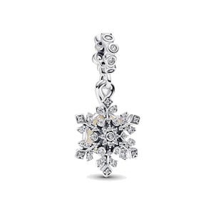 May include: A silver snowflake charm with clear crystals. The charm has a detailed snowflake design with a central circle and radiating points, all encrusted with sparkling crystals. The top portion features a series of smaller, crystal-studded accents.