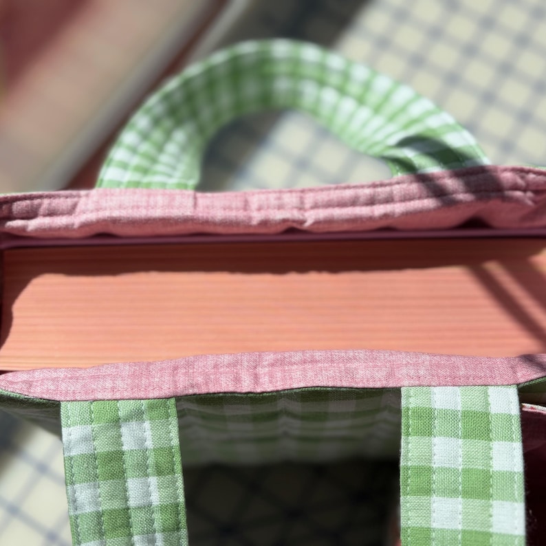 May include: Close-up of a handmade tote bag with a pink interior and a green and white checkered exterior. The bag has a pink trim and a matching checkered handle. The bag is made of fabric and has a rectangular shape.