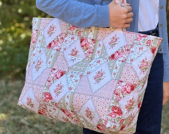May include: A large, quilted tote bag with a patchwork design. The bag features floral patterns in pink, red, and green on a white background. The bag has a matching strap and a pink zip. The bag is ideal for carrying items.