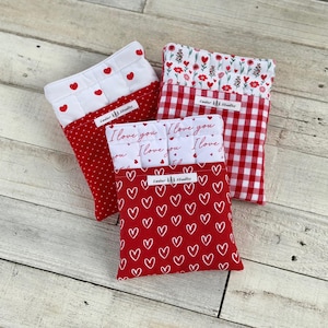 May include: Three fabric pouches with various patterns. One pouch has a red heart pattern, another has a red and white gingham pattern, and the third has a red polka dot pattern. The pouches have white tops with text that reads "I love you".