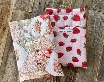May include: Two fabric pouches. One is patchwork with floral and geometric patterns in pink, white, and green. The other is light pink with a strawberry print. Both have a "Cedar Studios" label.