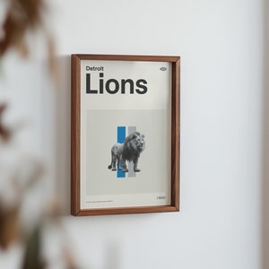 Op de afbeelding: Een ingelijste print met een bruine houten lijst. De print toont een zwart-wit afbeelding van een leeuw met blauwe en grijze strepen op de achtergrond. De tekst "Detroit Lions" is in zwart bovenaan de print gedrukt.