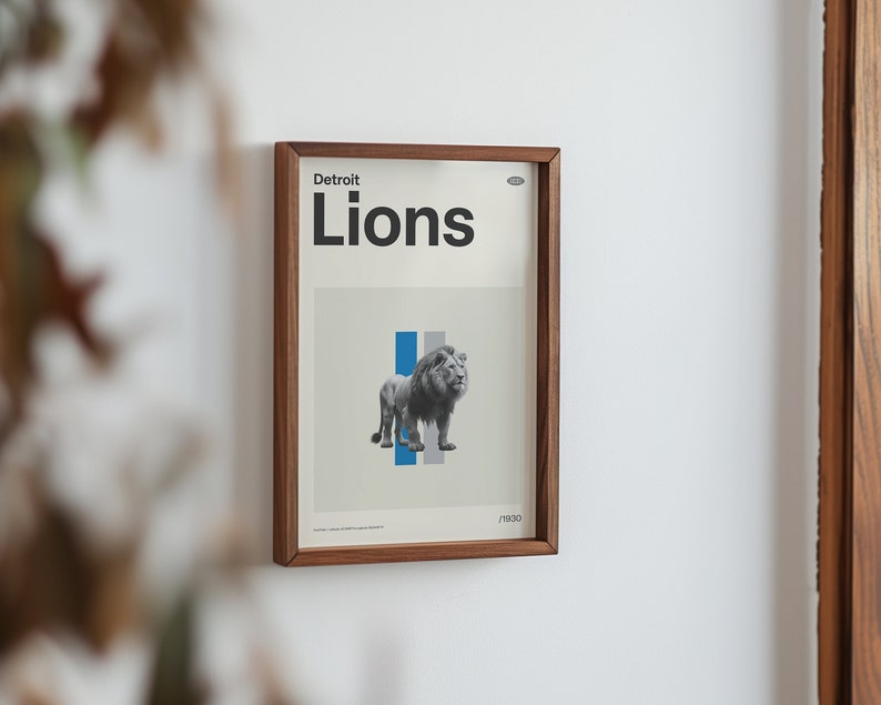 Op de afbeelding: Een ingelijste print met een bruine houten lijst. De print toont een zwart-wit afbeelding van een leeuw met blauwe en grijze strepen op de achtergrond. De tekst "Detroit Lions" is in zwart bovenaan de print gedrukt.