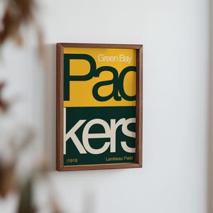 May include: A framed print with a green and yellow design. The text reads "Green Bay Packers" and "Lambeau Field".