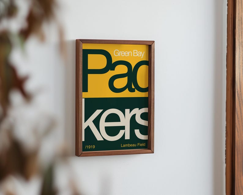 May include: A framed print with a green and yellow design. The text reads "Green Bay Packers" and "Lambeau Field".