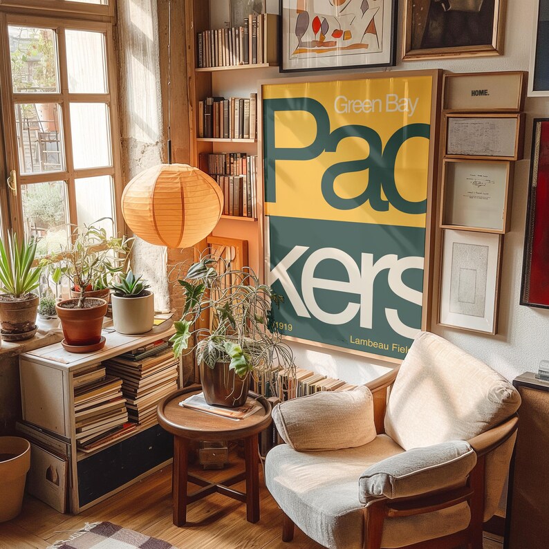 May include: A vintage Green Bay Packers poster with yellow and green text on a teal background. The poster is framed and hanging on a wall with bookshelves and other artwork.